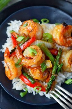 shrimp and asparagus stir - fry with rice on a black plate, ready to be eaten