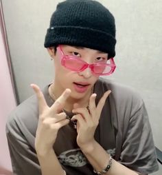 a young man wearing pink glasses making the peace sign with his fingers while sitting in front of a mirror