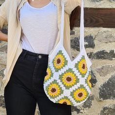 a woman holding a white purse with sunflowers on the front and side, standing in front of a stone wall