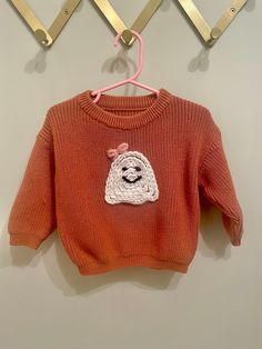 a red sweater with a white dog on it hanging from a clothes hook in front of a wall