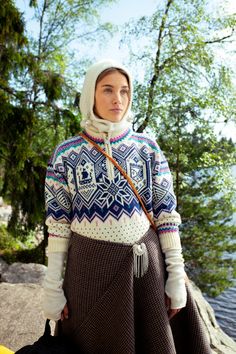 a woman is standing by the water wearing a sweater and skirt with an ornament on it