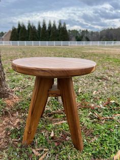 a small wooden table sitting in the middle of a grass covered field next to a tree