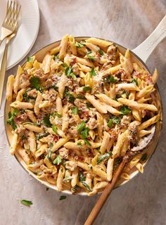 a pan filled with pasta and meat on top of a table next to silverware