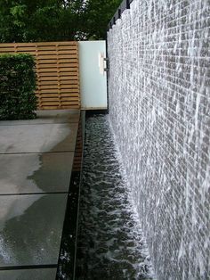 water gushing down the side of a wall in front of a wooden fence and shrubbery