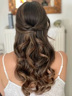 the back of a woman's head with long wavy hair in half updo