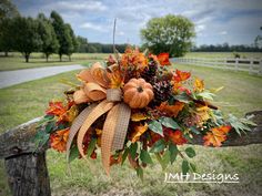 an arrangement of fall leaves and pumpkins on a wooden fence with a road in the background