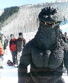 a group of people standing next to each other in front of a large godzilla costume