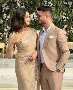 a man and woman standing next to each other in front of a flower covered wall