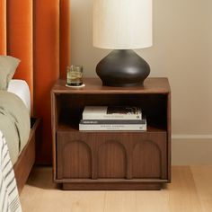 a nightstand with a lamp on top of it next to a bed