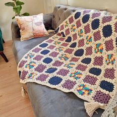 a crocheted granny blanket is sitting on a couch next to a potted plant