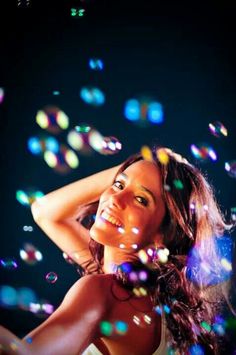 a woman standing in front of bubbles with her hand on her head and looking up