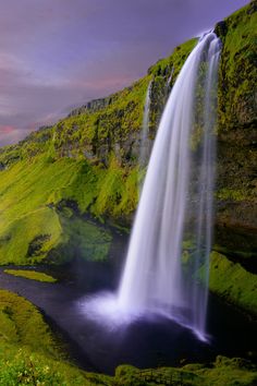 a large waterfall in the middle of a lush green hillside with water running down it's side