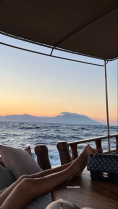 a woman laying on the back of a boat in the ocean at sunset with her feet up