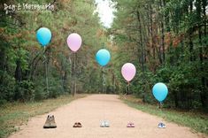 several blue and pink balloons floating in the air on a dirt road surrounded by trees