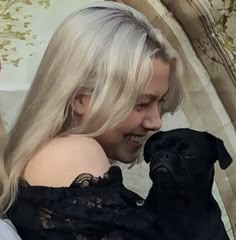 a woman holding a black pug in her arms and looking at it's face