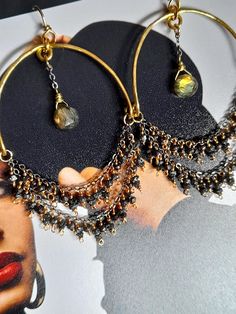 These gorgeous hoop earrings showcase hand formed and hammered moon shape frame bottomed with golden flash Labradorite drops and a gold filled chain embellished with little sparkly rough black Diamonds, all meticulously wired with a gold filled wire to make an unique round hoops, hanging on hand-formed brass ear wire. This pair of earrings is lightweight but very eye catching and one-of-a-kind. The earrings measure 3.1 inches (8cm) from the top of the ear wire to the bottom of the Diamond beads. The frame's width is approx. 1.6 inches (4cm). Handmade Fusion Chandelier Drop Earrings, Handmade Fusion Style Chandelier Drop Earrings, Handmade Spiritual Crescent Earrings, Festival Brass Wire Wrapped Hoop Earrings, Artisan Hoop Pierced Earrings, Artisan Hoop Pierced Jewelry, Handmade Bohemian Sterling Silver Wrap Earrings, Bohemian Hammered Teardrop Jewelry, Hand Forged Bohemian Hoop Jewelry