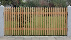 a wooden fence is shown in front of a brick wall and grass area with trees behind it