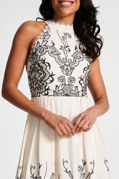 Step into spring with Zalie! Cut in a classic fit and flare silhouette, complete with a halter style neckline, this darling off-white midi dress is embroidered with contrasting black embroidery, realised in a lace motif. High Neck Cream Dress For Spring, Elegant Fitted Maxi Dress With Embroidered Neckline, Elegant White Embroidered Midi Dress, Elegant Midi Embroidered Dress With Lace Trim, White Embroidered Maxi Dress For Evening, White Embroidered Midi Dress For Party, Elegant Spring Maxi Dress With Embroidered Neckline, Elegant Embroidered Dress With Neckline Detail For Summer, Elegant Summer Dress With Embroidered Neckline