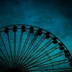 a large ferris wheel sitting under a cloudy blue sky at night with the moon in the distance