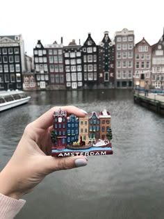 a person holding up a small card in front of a body of water with buildings on it