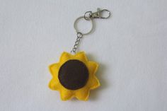 a yellow and brown felt sunflower keychain hanging from a metal hook on a white surface