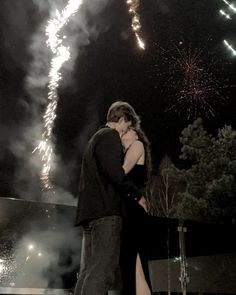 a man and woman standing next to each other with fireworks in the background