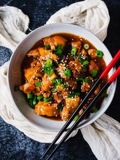 a white bowl filled with meat and vegetables next to chopsticks on a blue surface