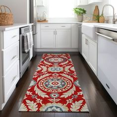 a kitchen with white cabinets and red rugs on the floor in front of an oven