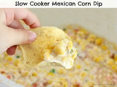 a hand holding a tortilla chip over a casserole dish filled with mexican corn dip