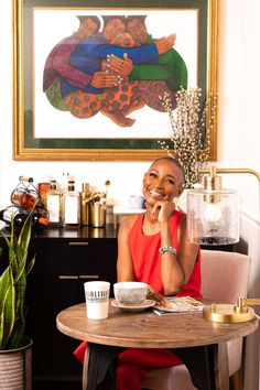 a woman sitting at a table in front of a painting and coffee cup on the side