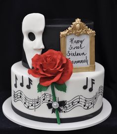 a cake with music notes and a red rose on the bottom layer, topped with a white mask