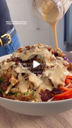 a person pouring gravy on top of a salad in a bowl with carrots