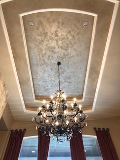 a chandelier hanging from the ceiling in a room with red drapes and curtains