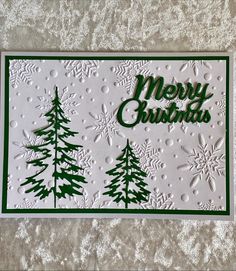 a white card with green trees and snowflakes on it, that says merry christmas