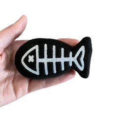 a hand holding a rock with a fish painted on it's side, in front of a white background