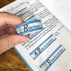 a hand holding a blue and white ribbon with writing on it next to an open notebook