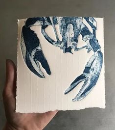 a hand holding up a piece of paper with blue and white images of crabs on it