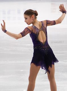 a female figure skating on an ice rink wearing a purple dress with sequins