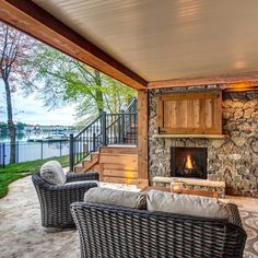 an outdoor living area with wicker furniture and stone fireplace on the deck overlooking water