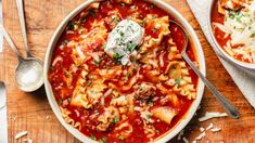 two bowls of pasta and meat soup on a cutting board