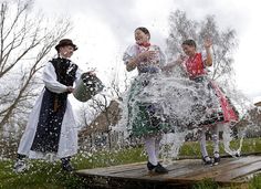 three people dressed in historical clothing splashing water on each other while standing on a wooden platform