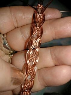 a person holding onto a chain that is in the palm of their hand and it looks like they are making something out of copper wire