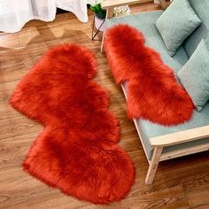 two red fur rugs sitting on top of a wooden floor next to a couch