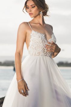 a woman in a white dress is standing near the water with her hand on her hip