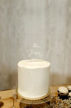 a white frosted cake sitting on top of a table next to cupcakes