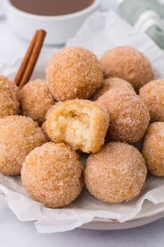 some sugared doughnuts on a plate with cinnamon sticks and a cup of coffee