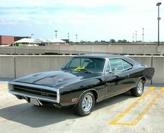 a black muscle car parked in a parking lot next to a cement wall and yellow lines