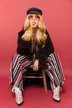 a woman sitting on top of a wooden chair holding a drink in her hand and wearing striped pants