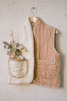 two vests hanging on a wall with flowers in the pocket and one has a flower pot inside