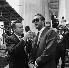 two men in suits standing next to each other and one is holding something with his hand